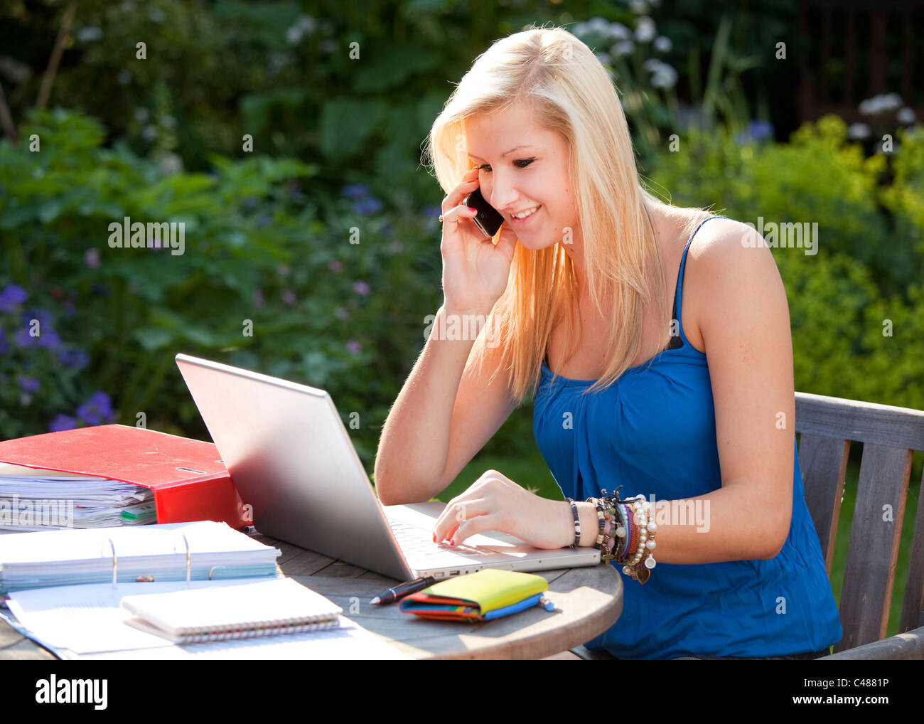 Young girl Chatting on moblie phone while on the internet, socializing on wireless laptop computer in the garden Stock Photo