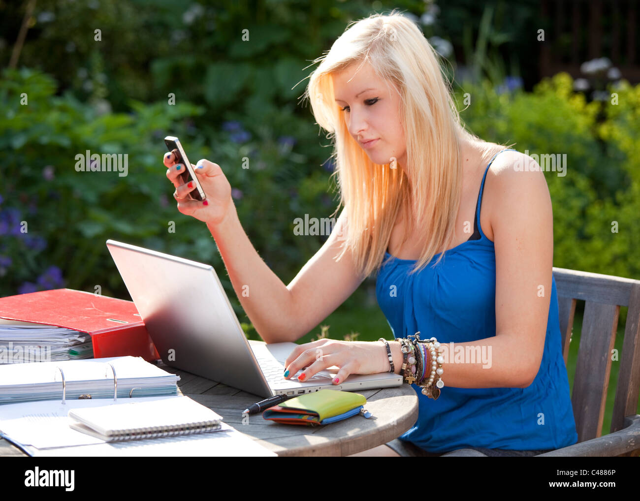 young girl texting on moblie phone while on laptop computer socializing outside in the garden Stock Photo