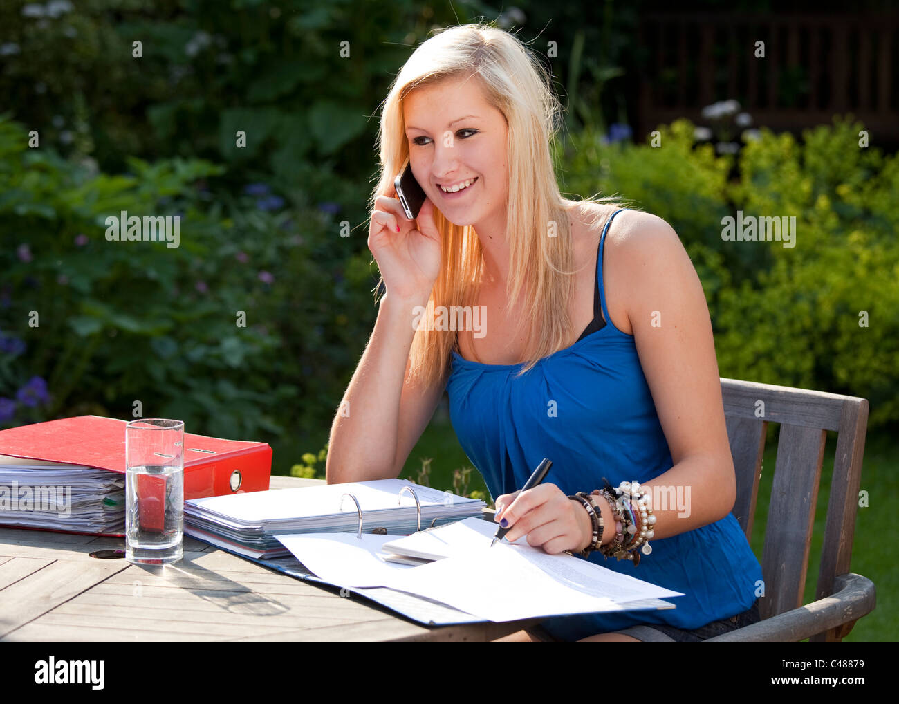 Happy teenage girl student working and chatting on moblie phone in garden Stock Photo