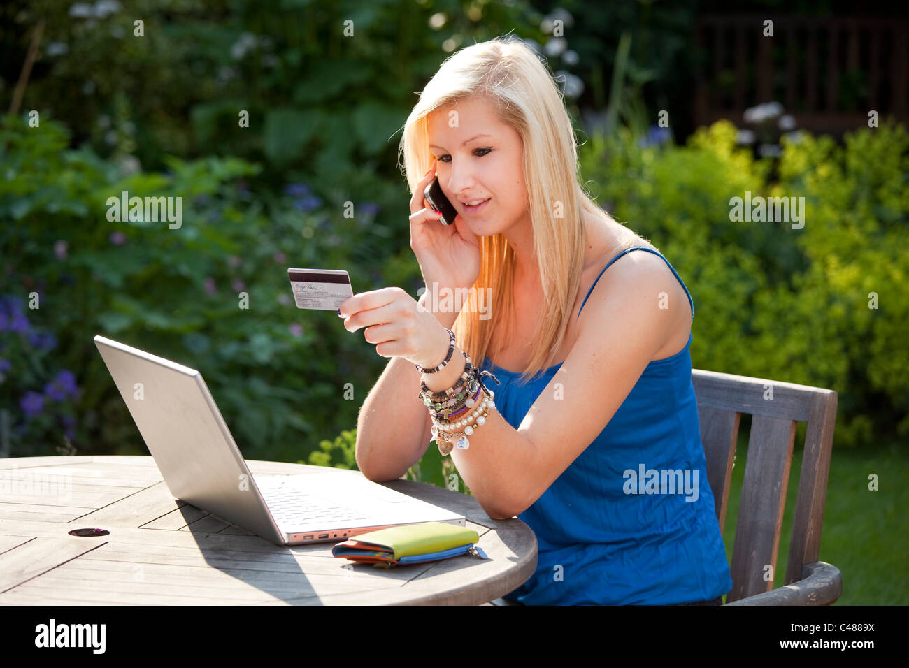 Young girl talking on moblie phone online shopping with credit card in the garden on a wireless laptop computer Stock Photo