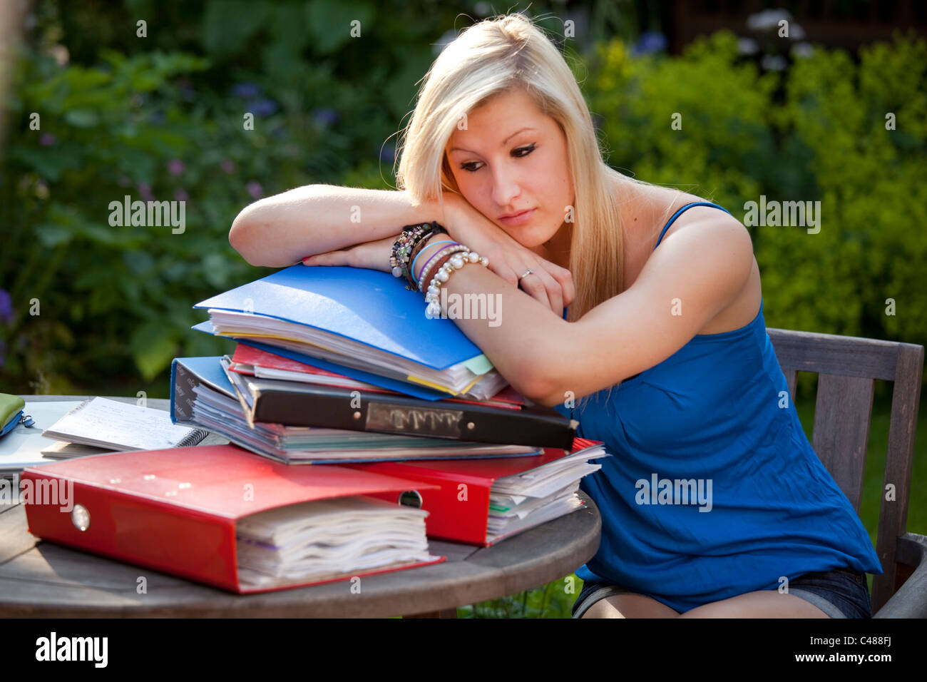 Young girl stressed with revision in garden with files and books ready to study  for exams Stock Photo