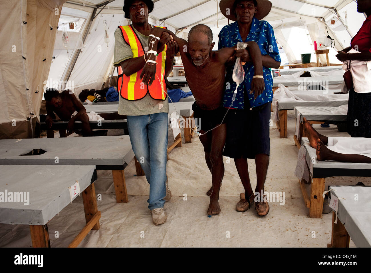 Elderly man weakened by cholera disease is being helped to a bed in tent hospital. Stock Photo