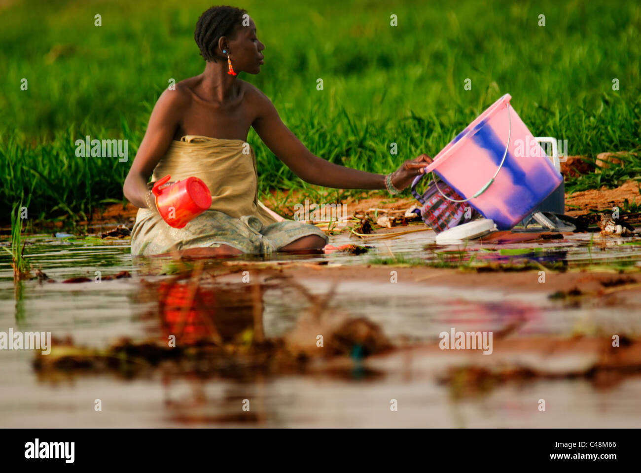 A Songhai woman kneeling in mud washing clothes in the Niger River, Gao