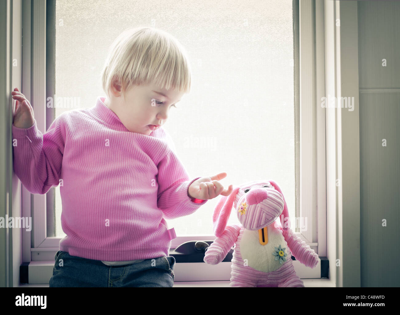Little girl sitting on the window pane looking at her favorite toy Stock Photo Alamy