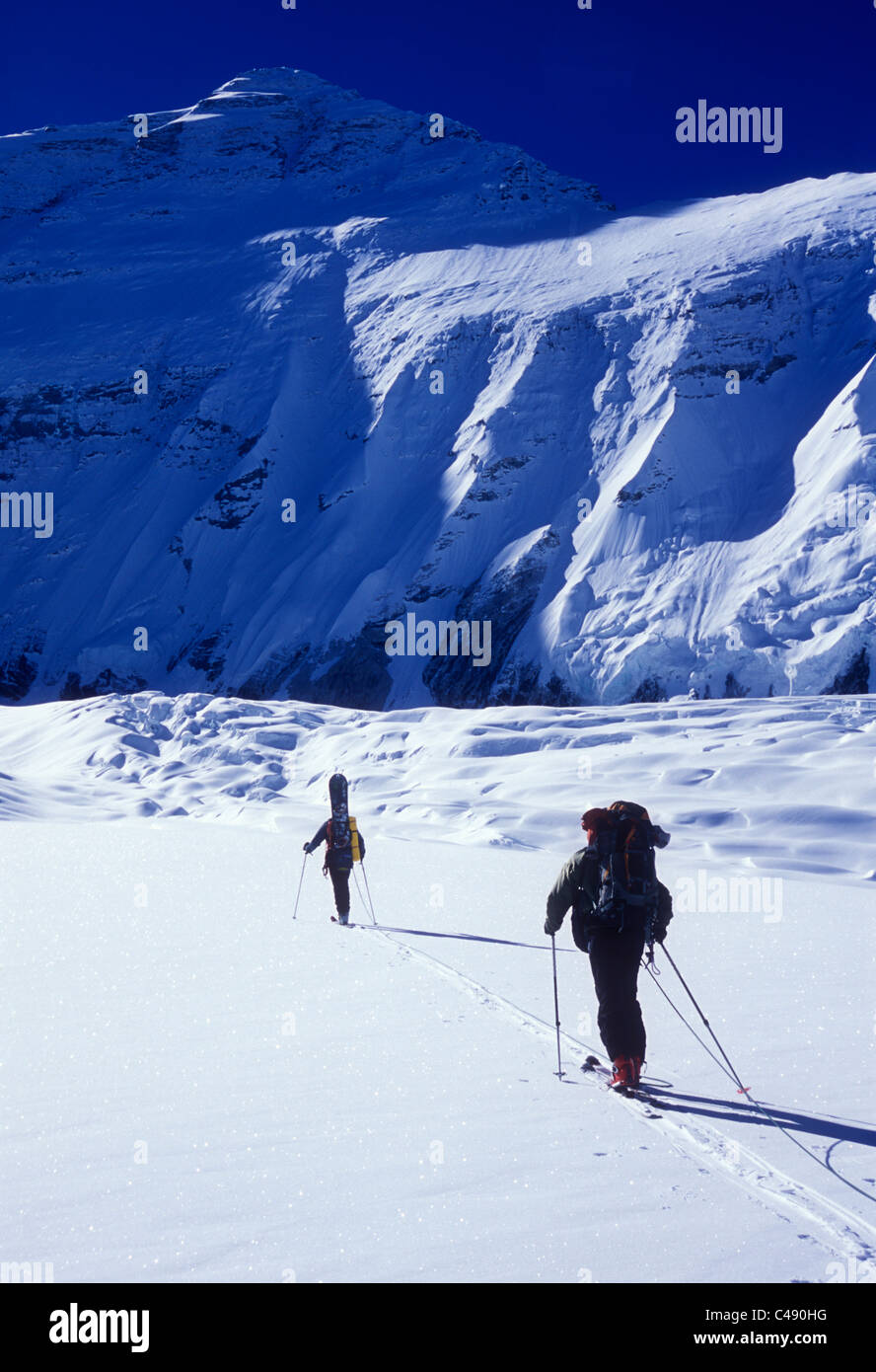 Two men ski touring under sunny skies in the shadow of the north face of Mount Everest. Stock Photo