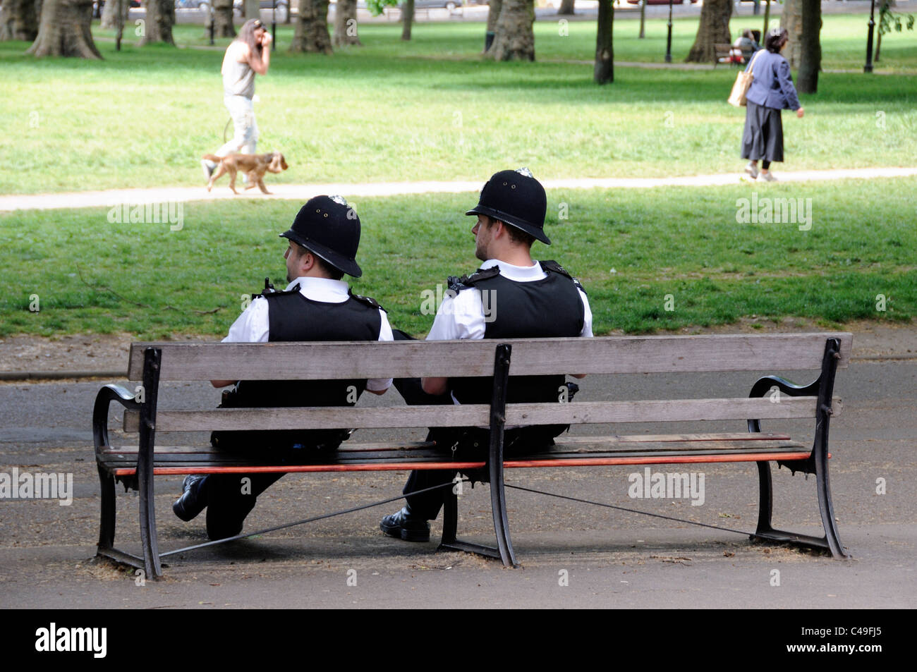 Bobbies sitting on a bench, two Metropolitan police officers watching activities on Highbury Fields in summer London England UK Stock Photo