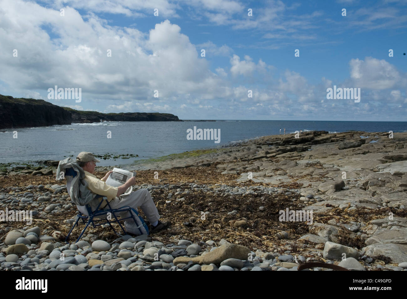 Photograph of a man reading a paper on a beach in Ireland Stock Photo