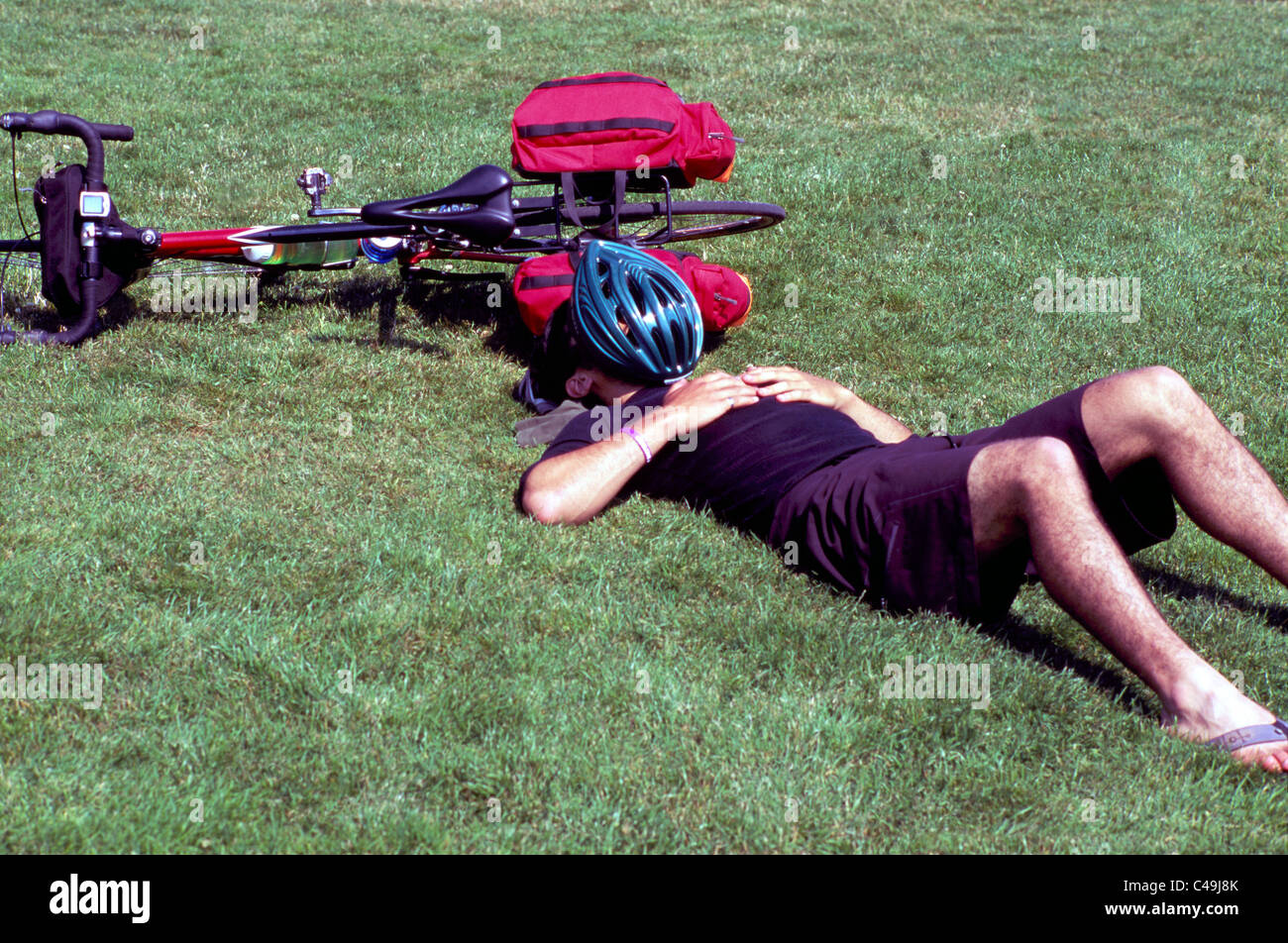 Cyclist lying on Back in Grass, Man Asleep on Ground and Taking it Easy beside Bicycle Stock Photo