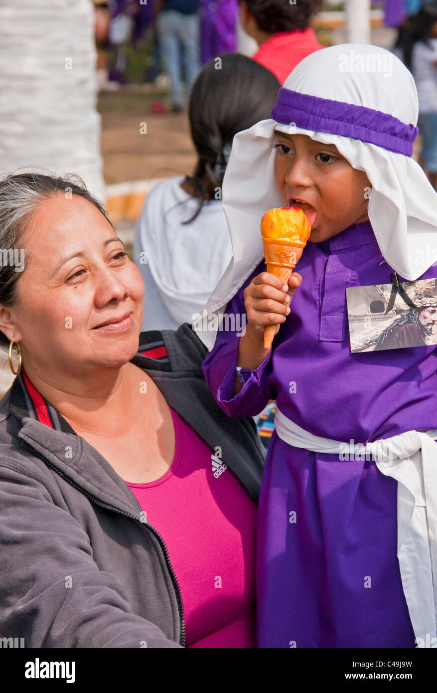 Holy Week (Semana Santa) in Antigua with child eating ice cream wearing purple rebes as participant in the annual observance Stock Photo