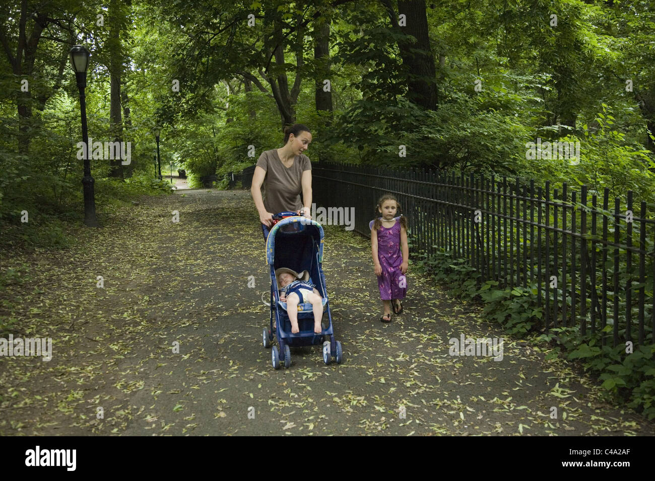 4 year old girl walks with mom as she pushes stroller with 1 year old inside. Riverside Park, NYC. Stock Photo