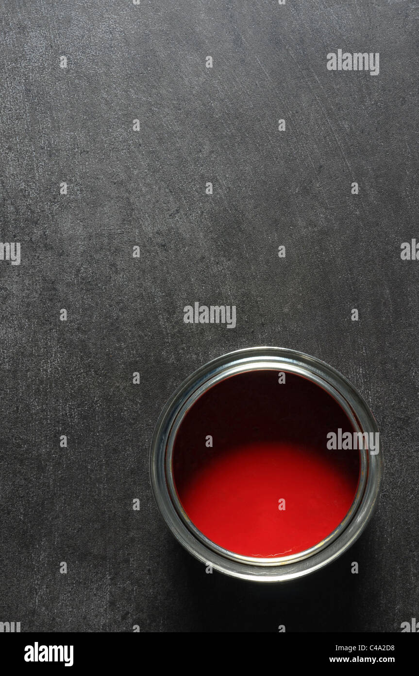 open tin of vibrant gloss red paint on grey slate floor background