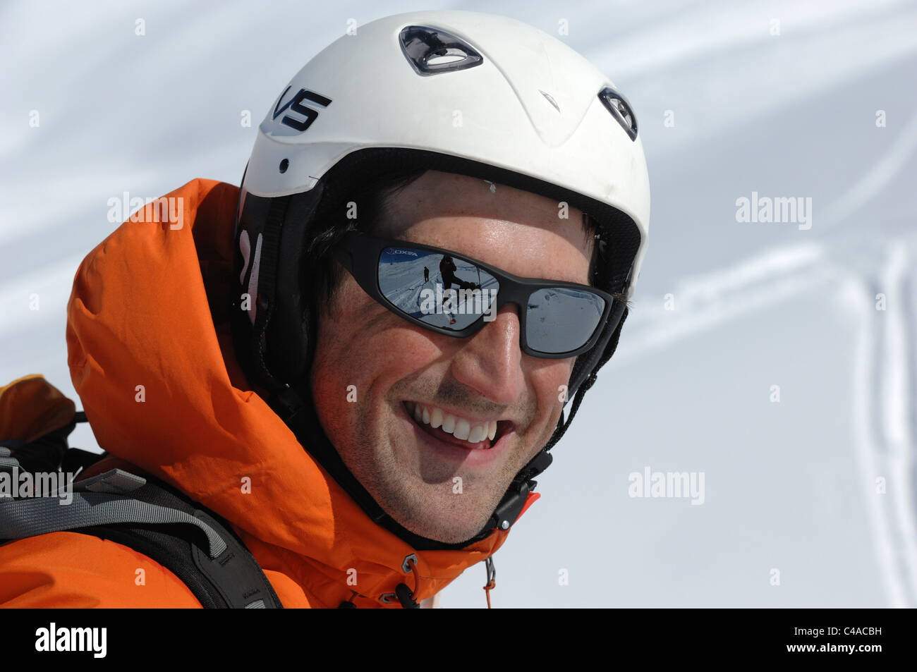 A close up of a happy male skier smiling wearing a orange jacket  helmet and sunglasses on a clear sunny day Stock Photo