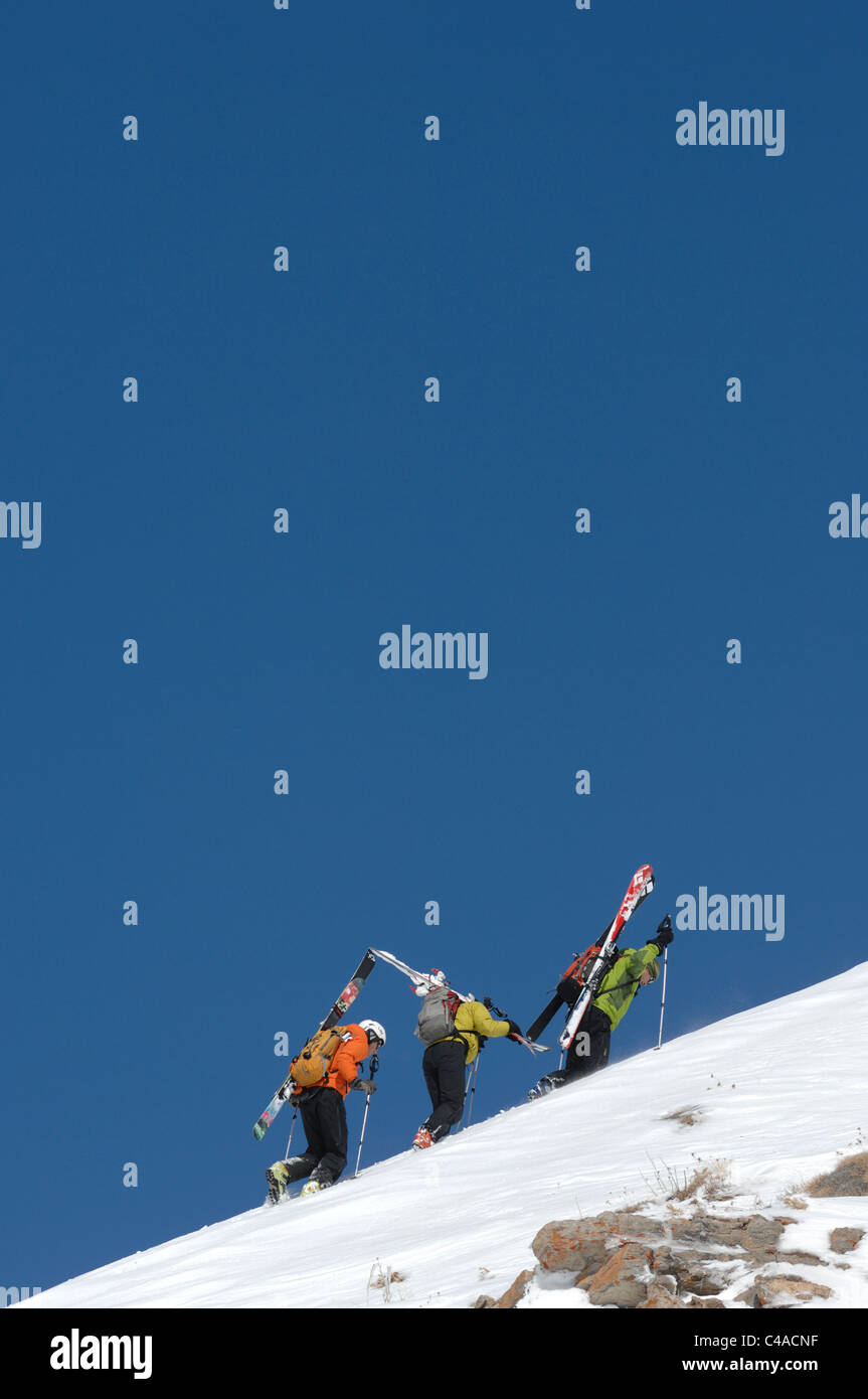 Three backcountry ski mountaineers carrying skis on a snow covered ridge line against  a deep blue sky in Dizin Iran Stock Photo
