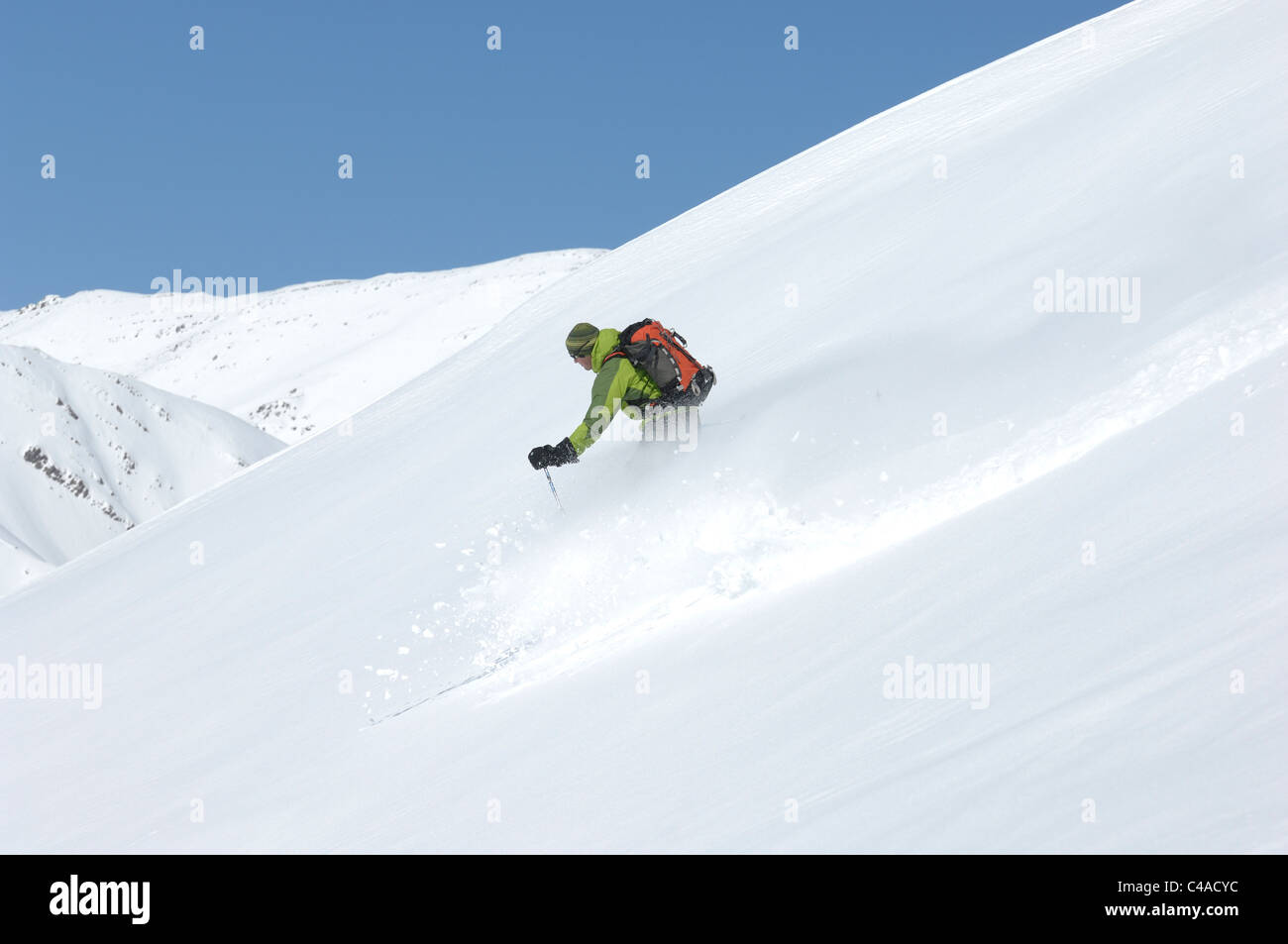 A man skiing wearing a rucksack off piste in fresh snow under a blue sky in Dizin resort part of the Alborz mountains Iran Stock Photo