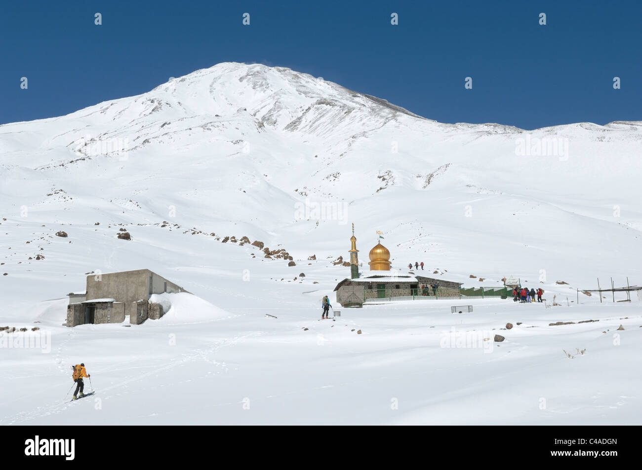A group of ski mountaineers skiing up to the Saheb al Zaman Mosque on Mt Damavand in the Alburz mountains of Iran in winter. Stock Photo