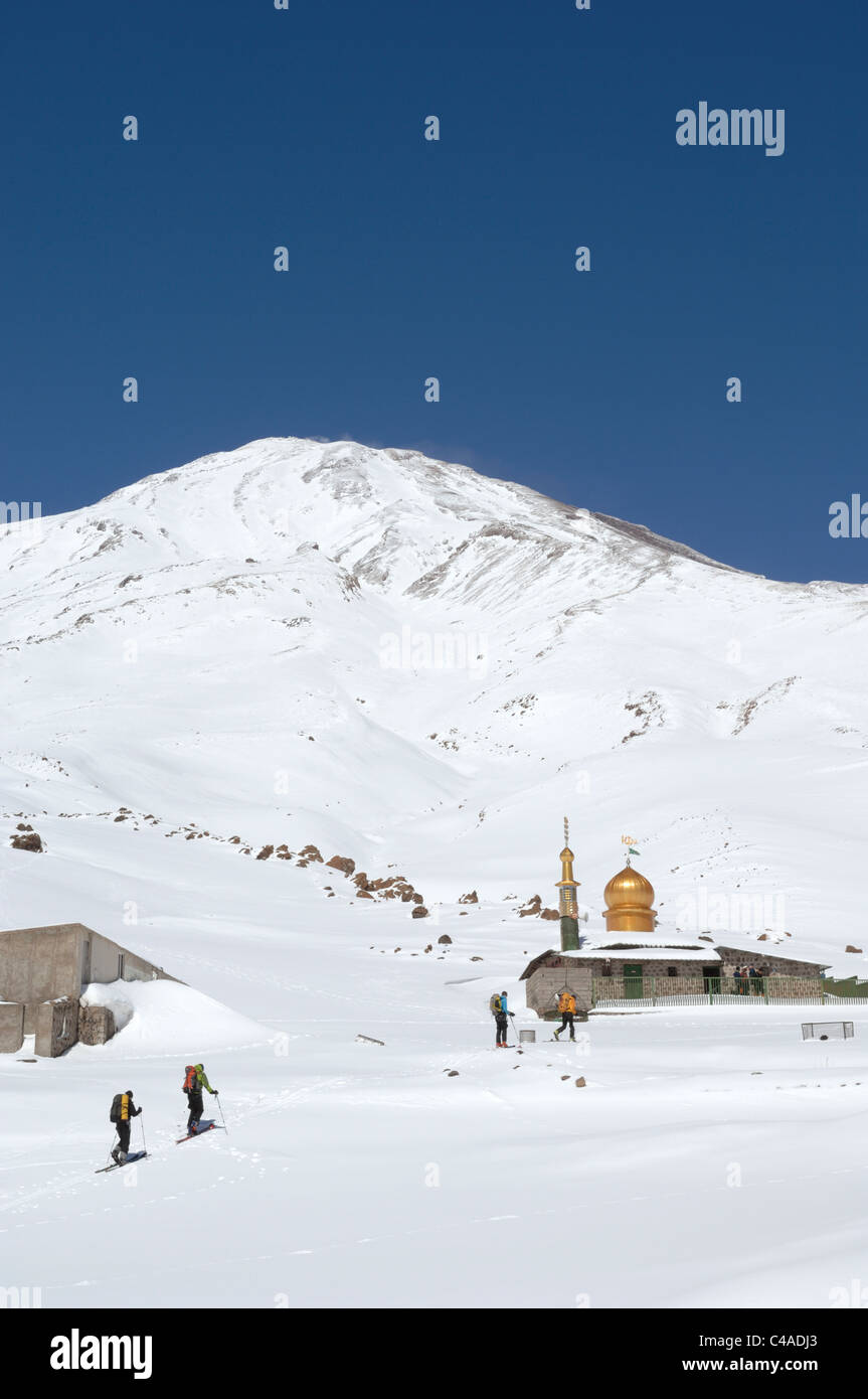 A group of ski mountaineers skiing up to the Saheb al Zaman Mosque on Mt Damavand in the Alburz mountains of Iran in winter. Stock Photo