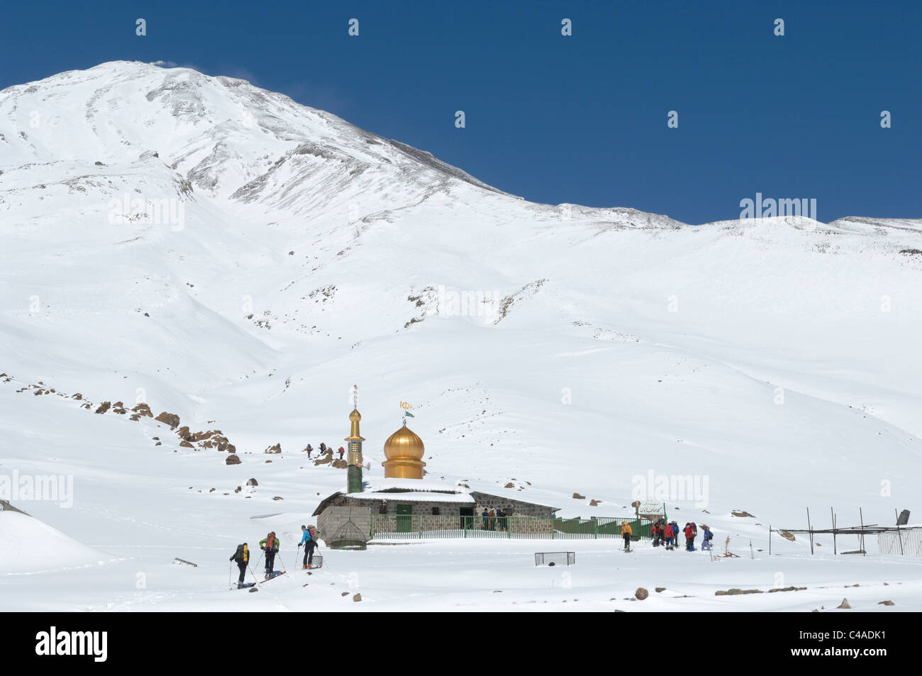 A group of ski mountaineers skiing up to the Saheb al Zaman Mosque on Mt Damavand in the Alburz mountains of Iran in winter. Stock Photo