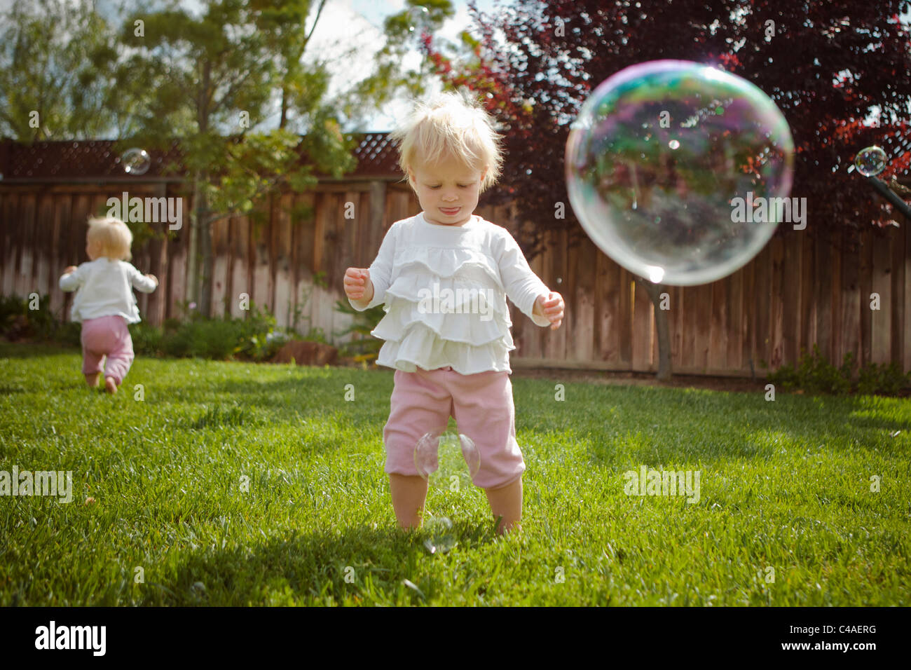 Twins Girls Outside on Grass Chasing Bubbles Stock Photo