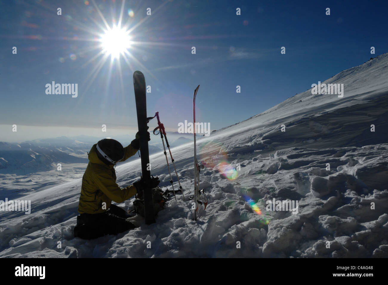 A silhouetted mountaineer fitting ski mountaineering climbing skins on