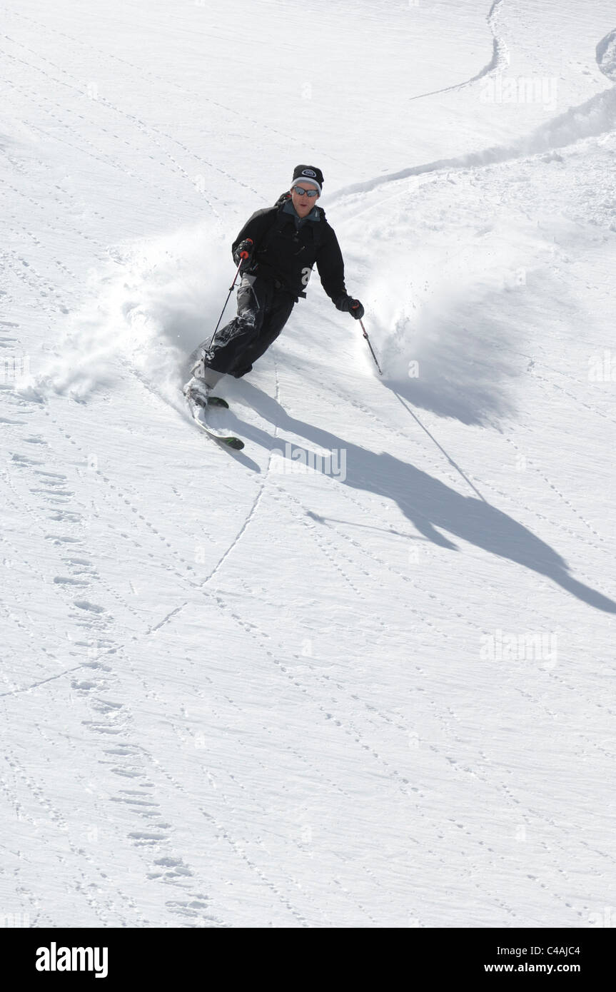 A man telemark skiing in deep fresh powder snow under a clear blue sky