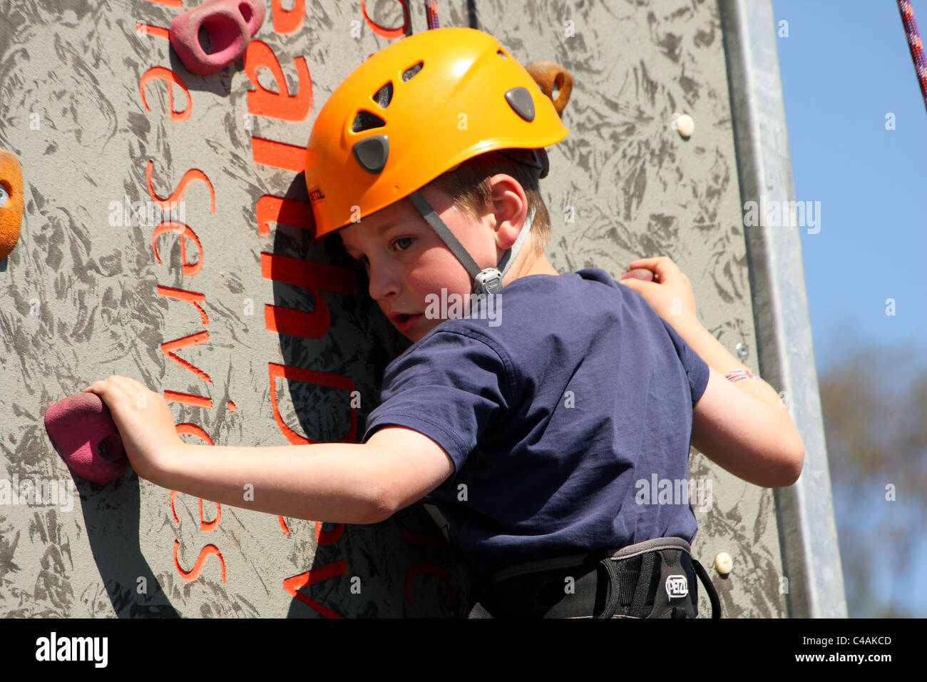 A young boy learning how to rock climb on a climbing wall outside in