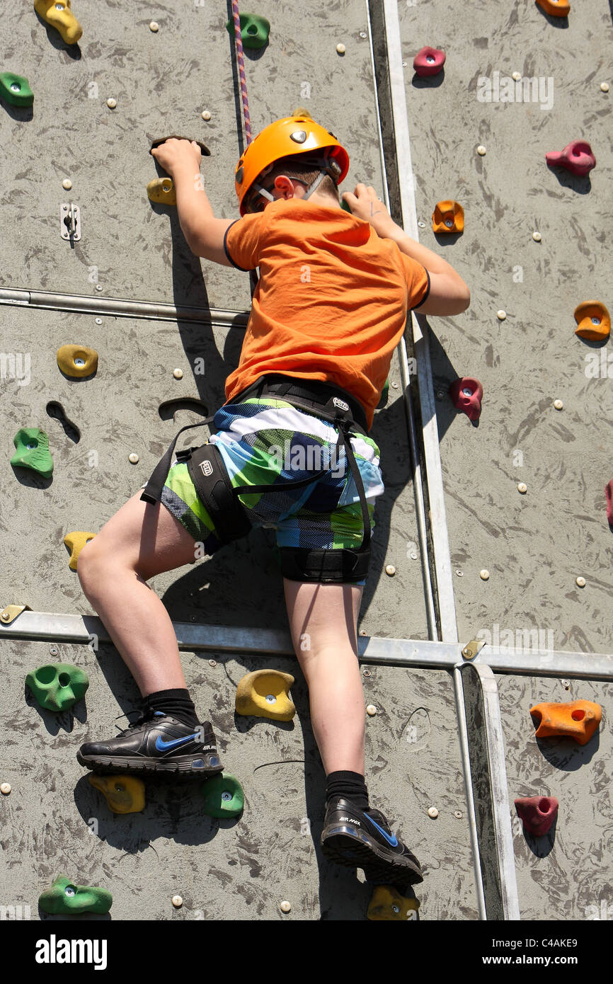 A young boy learning how to rock climb on a climbing wall outside in