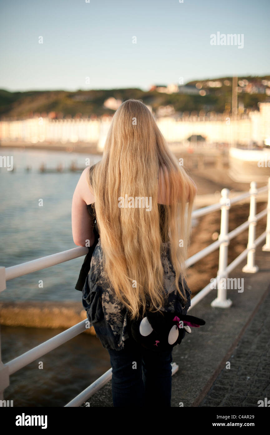 A rear view of a woman with very long blonde hair standing on ...