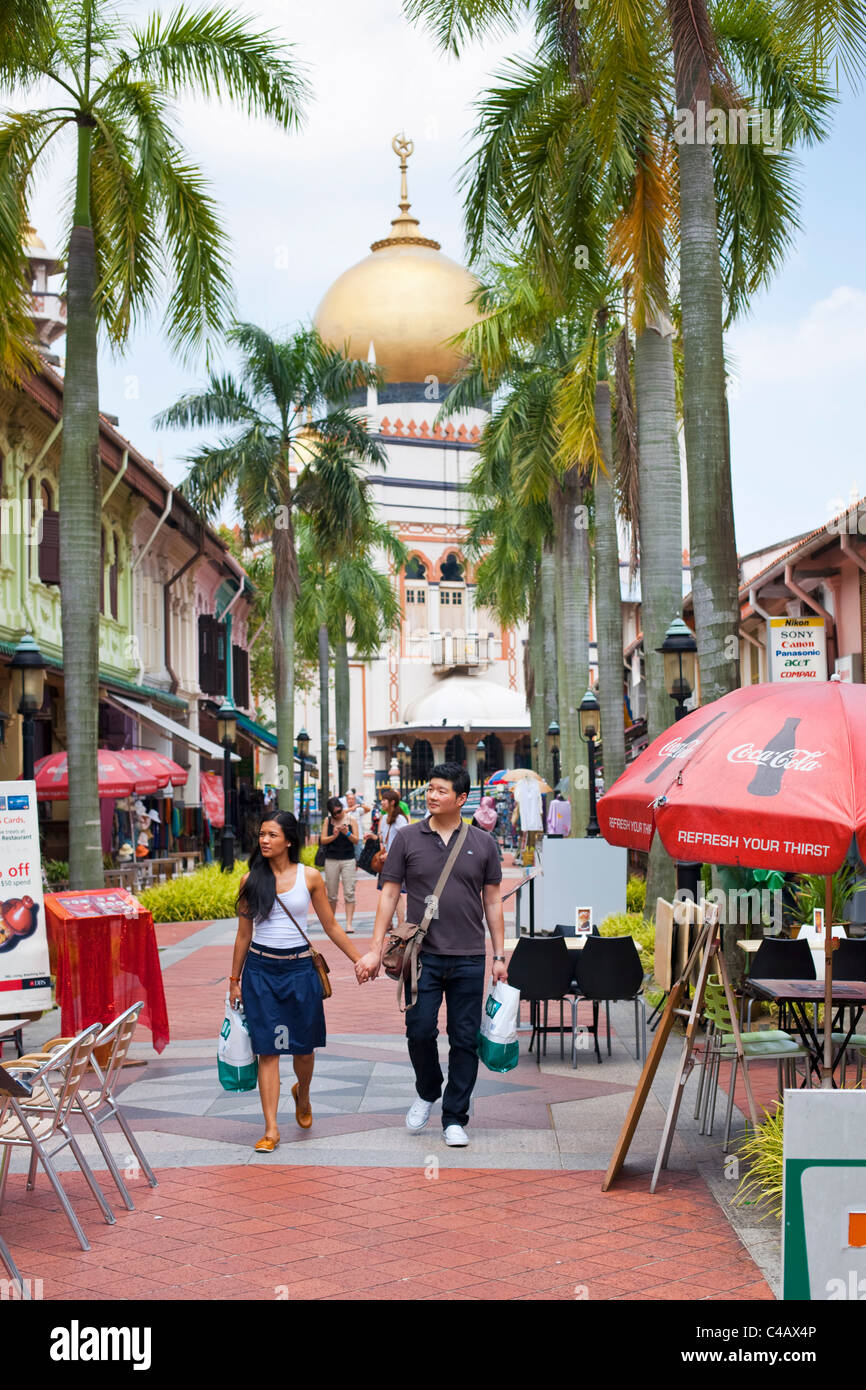 Singapore, Singapore, Arab Quarter. Couple walking along Bussorah Mall with Sultan Mosque in background. Stock Photo