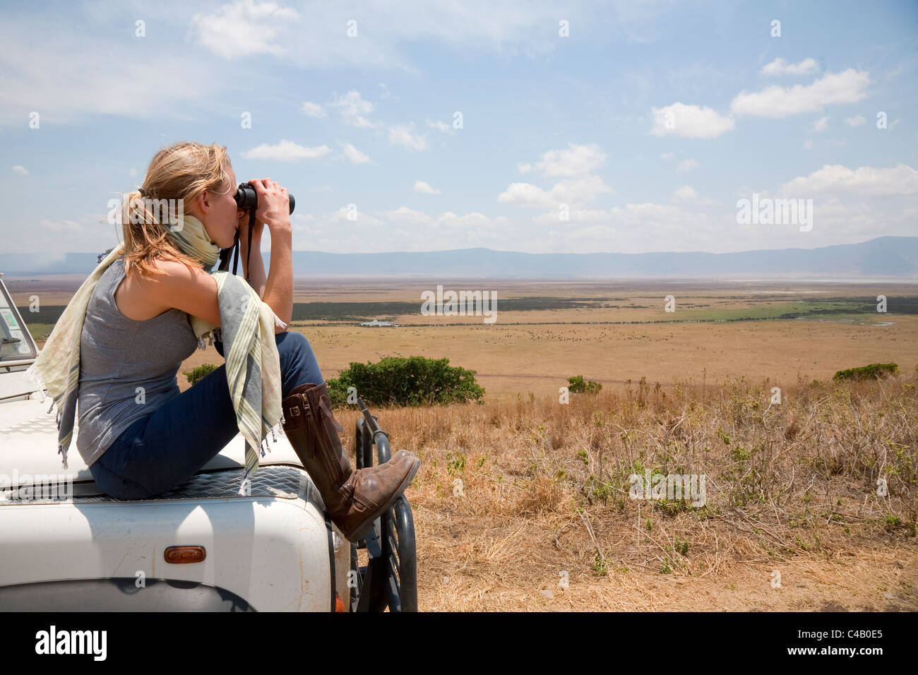 Tanzania, Ngorongoro. A tourist looks out over the Ngorongoro Crater from the bonnet of her Land Rover. MR. Stock Photo