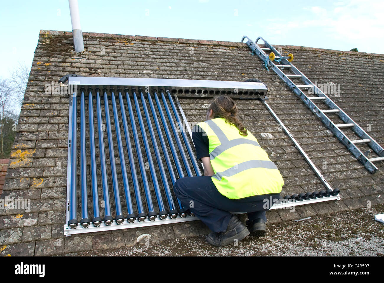 Engineers installing solar thermal evacuated tube array on the roof of a domestic house to provide renewable heat and hot water Stock Photo