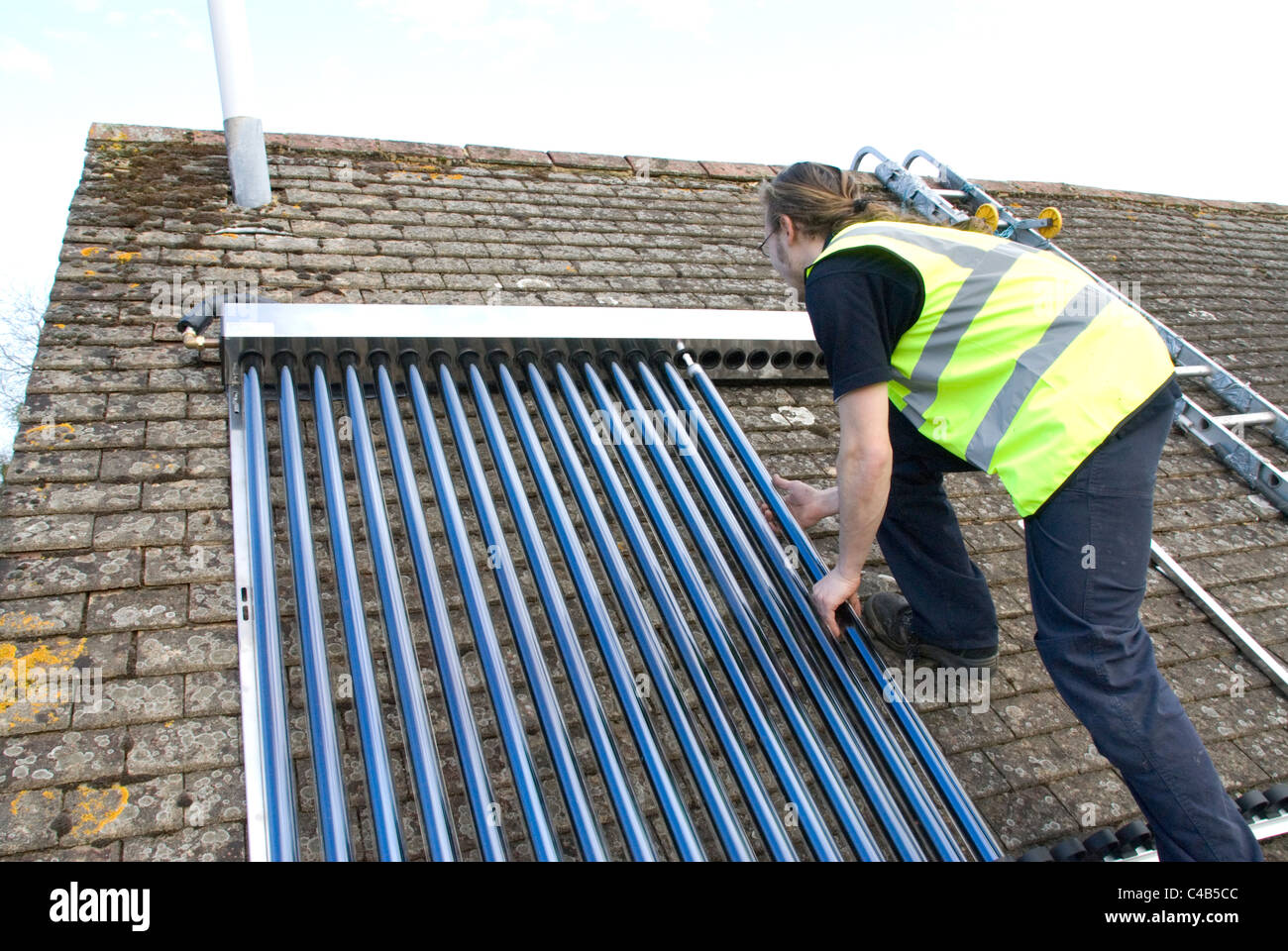 Engineers installing solar thermal evacuated tube array on the roof of a domestic house to provide renewable heat and hot water Stock Photo