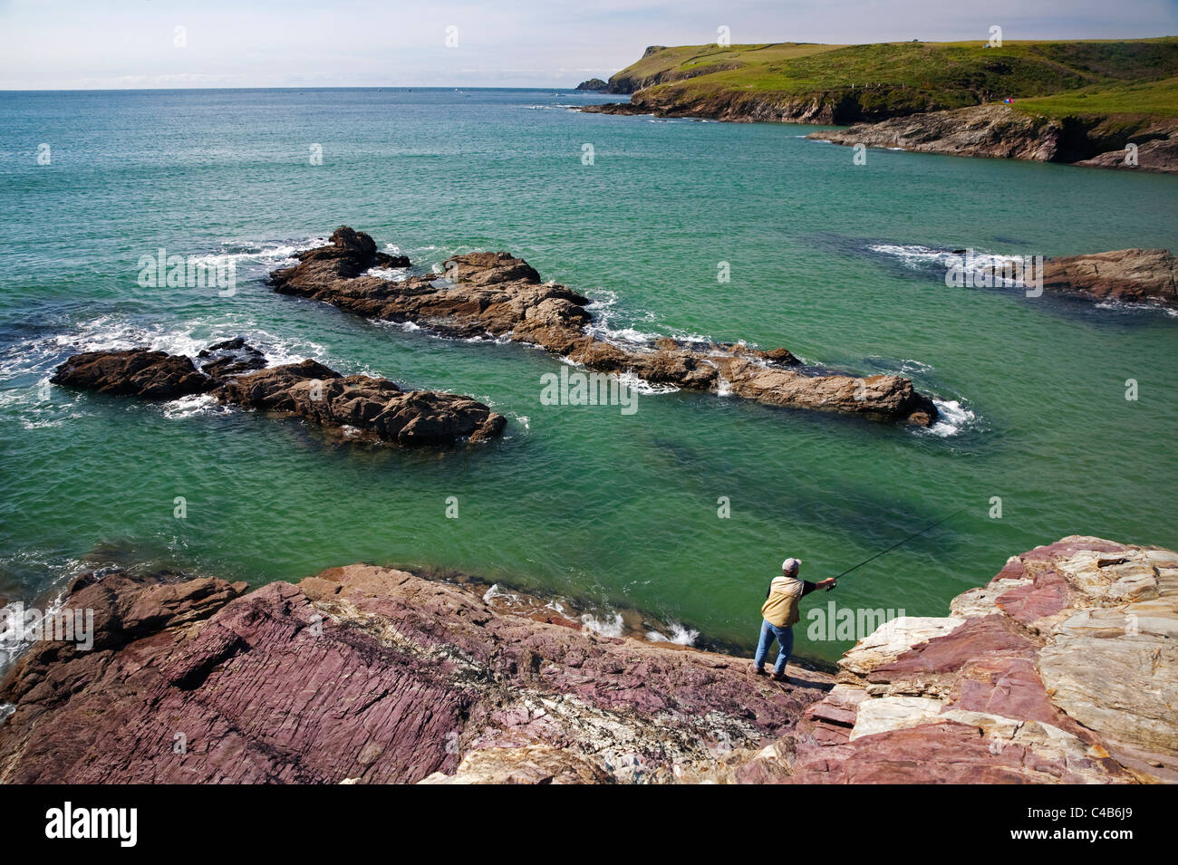 UK, Cornwall. A man fishes off the rocks near Polzeath. (MR) Stock Photo