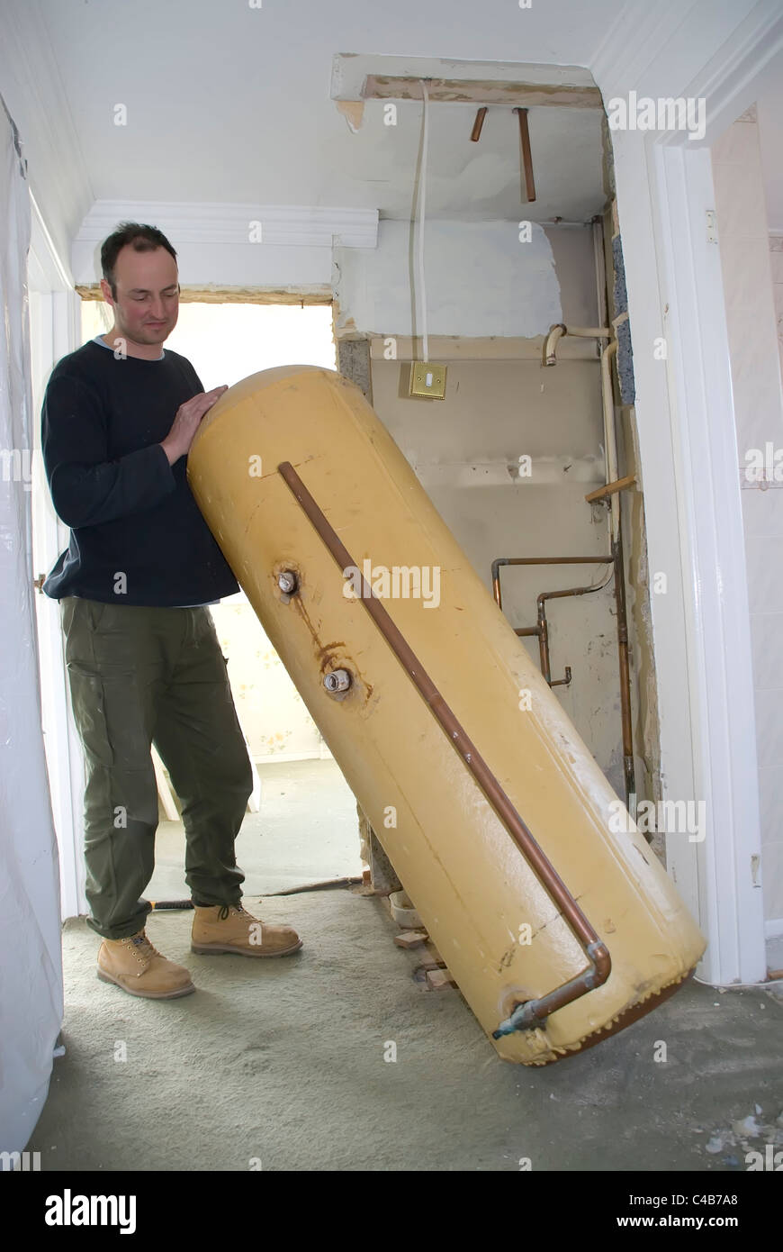 man removing hot water cylinder from house Stock Photo