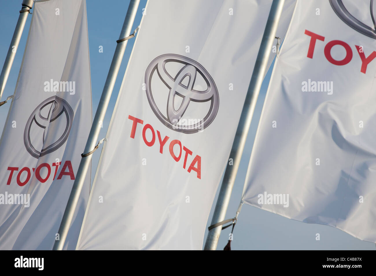 White Toyota brand flags on metal poles waving against a clear blue sky, showcasing the red Toyota logo and lettering Stock Photo