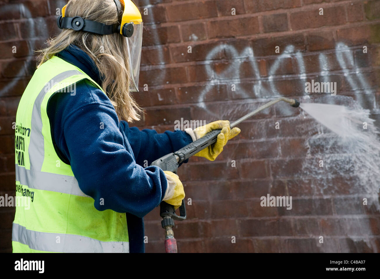 Council worker using a jet wash to clean graffiti off of a wall in