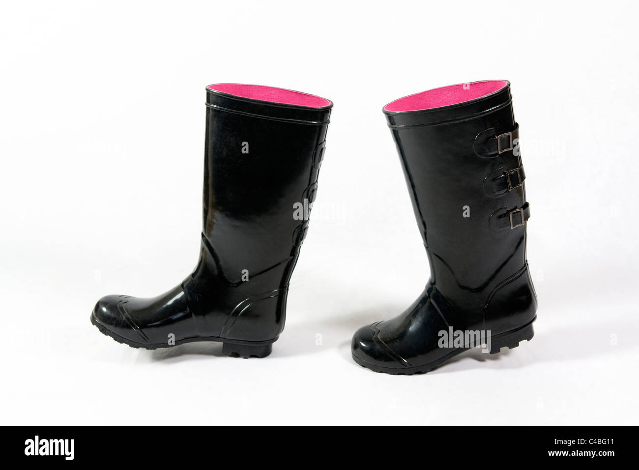 A pair of black wellies, or wellington boots with pink inside taken against a white background positioned as if they are walking Stock Photo