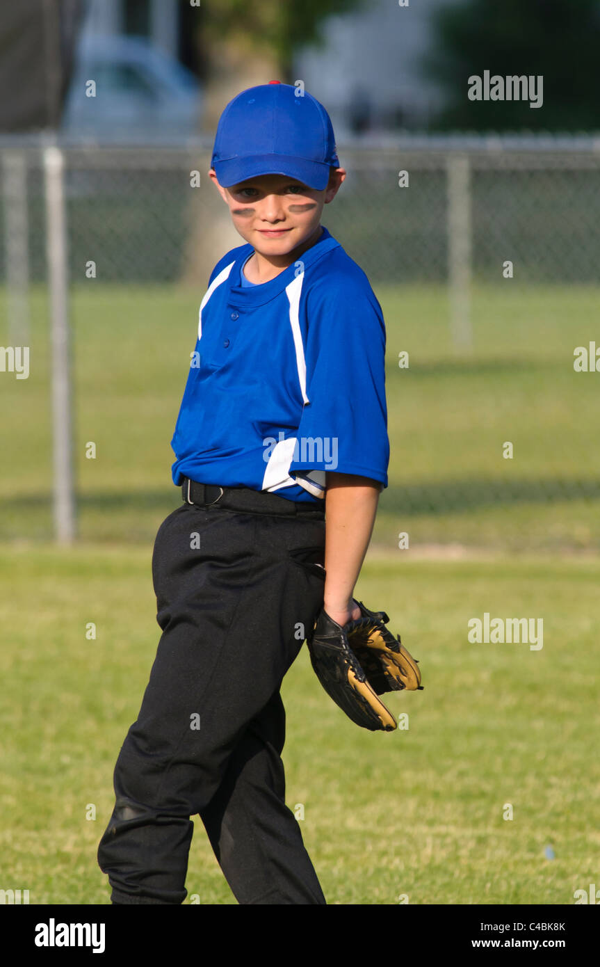 Little league baseball player poses in the field during a late summer