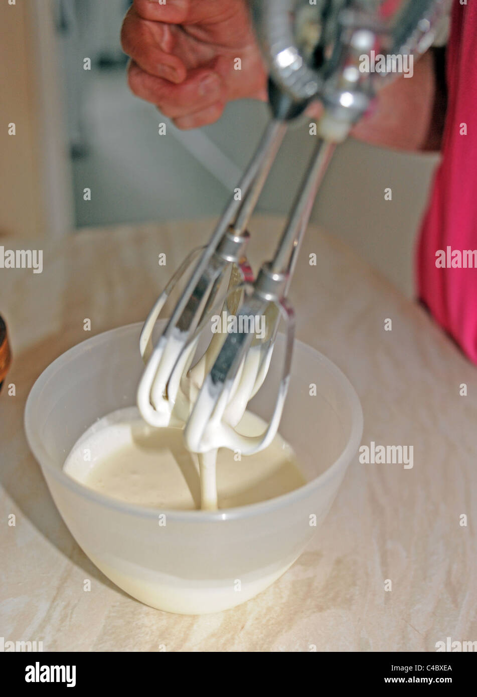 Woman using an old fashioned hand whisk in a bowl of cream in kitchen