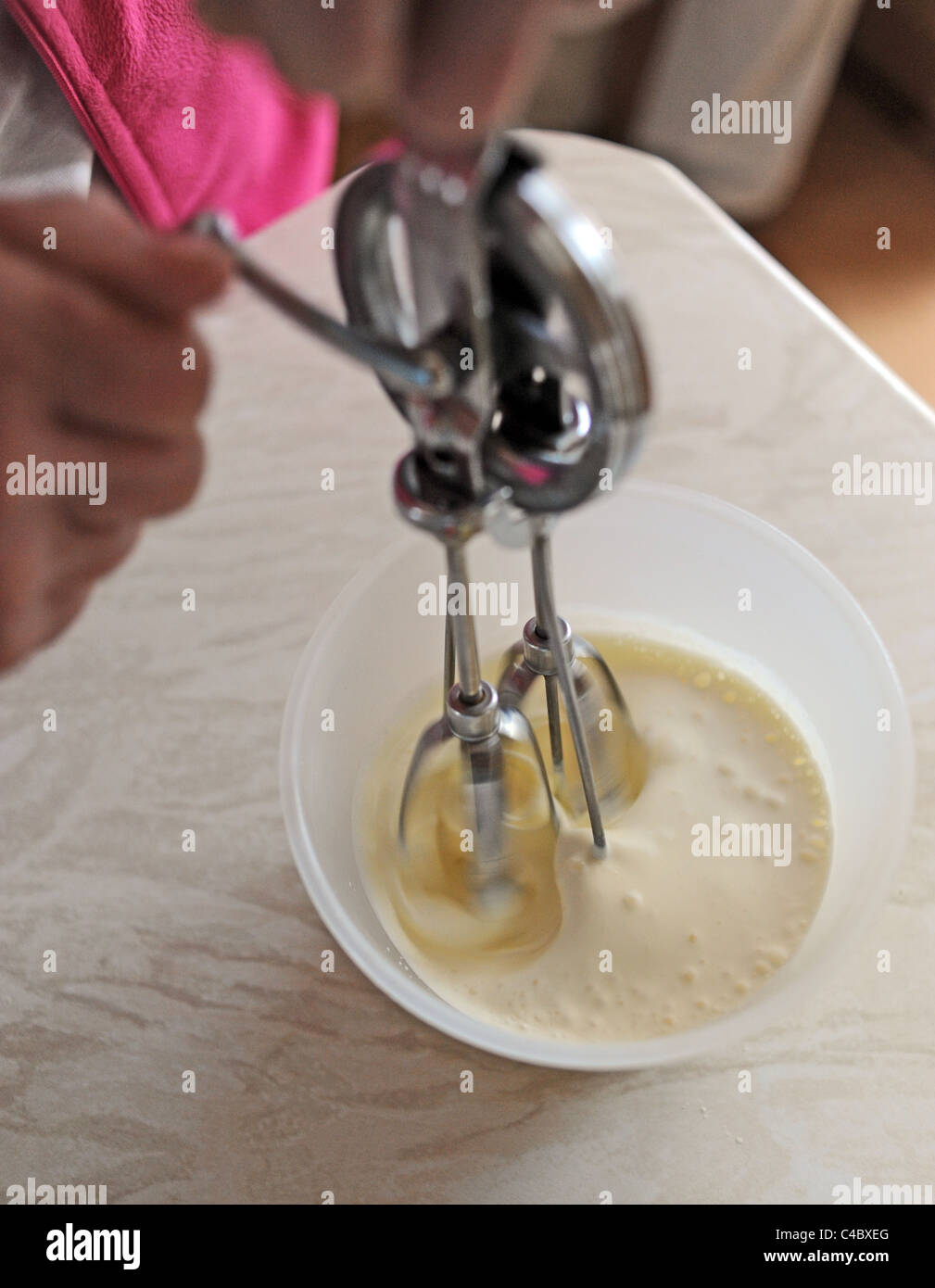 Woman using an old fashioned hand whisk in a bowl of cream in kitchen