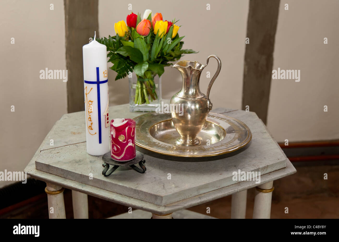 Requisites for Christening: baptism candle with the name Konrad, flowers, jug for baptismal water Stock Photo