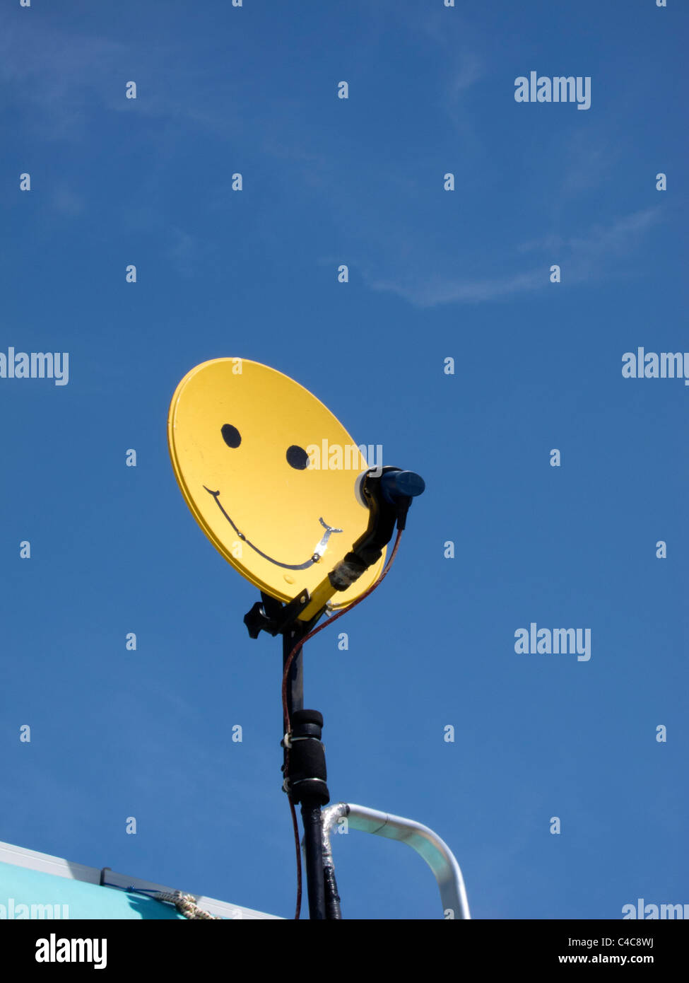 A brightly colored yellow satelite dish with a smiley face on it set against a blue sky. Stock Photo