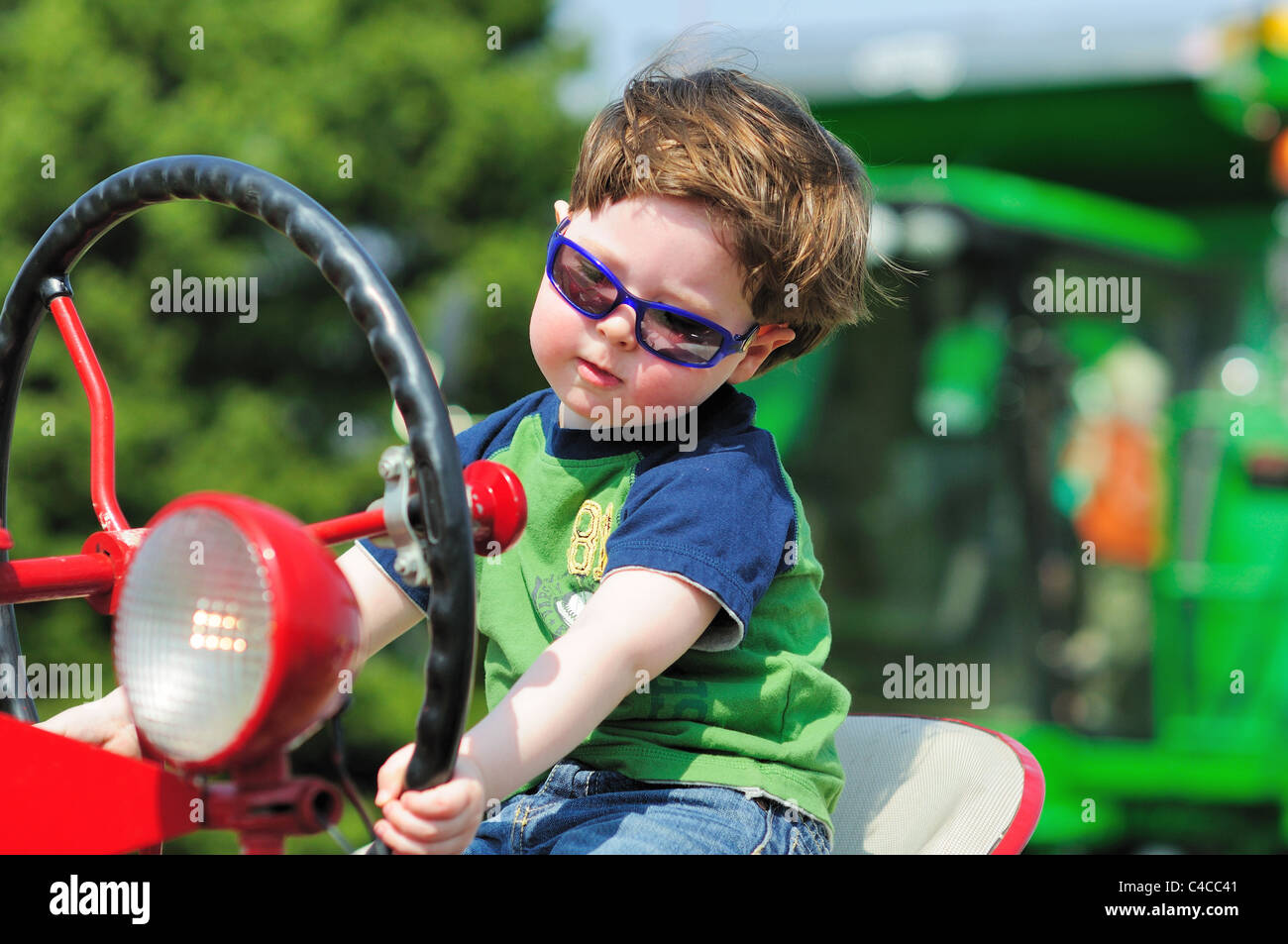 Little boy sits on an antique tractor as he enjoys an imaginary ride at a local farm bureau touch a tractor event. St. Charles, Illinois, USA. Stock Photo