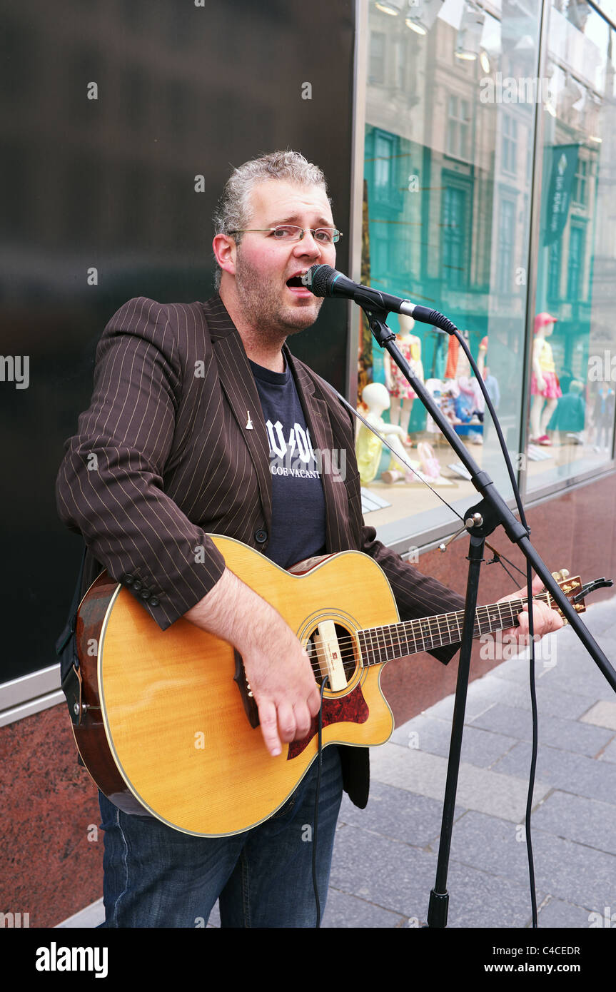 Adult male busking by playing the guitar and singing in Buchanan Street, Glasgow, Scotland Stock Photo