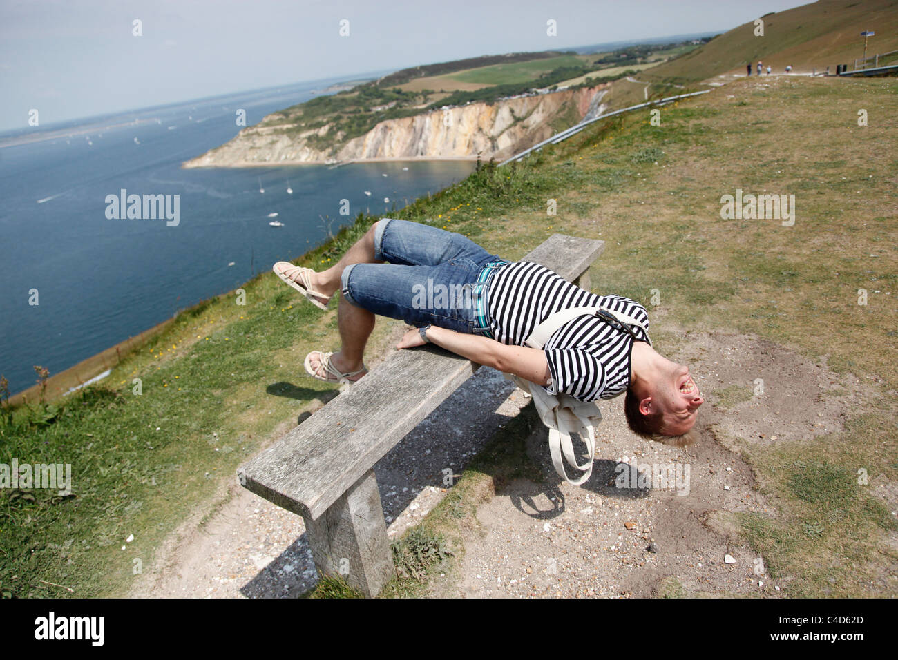 Man wearing striped T shirt on holiday leaning back on a cliff top bench having fun and stretching - Model Released Stock Photo