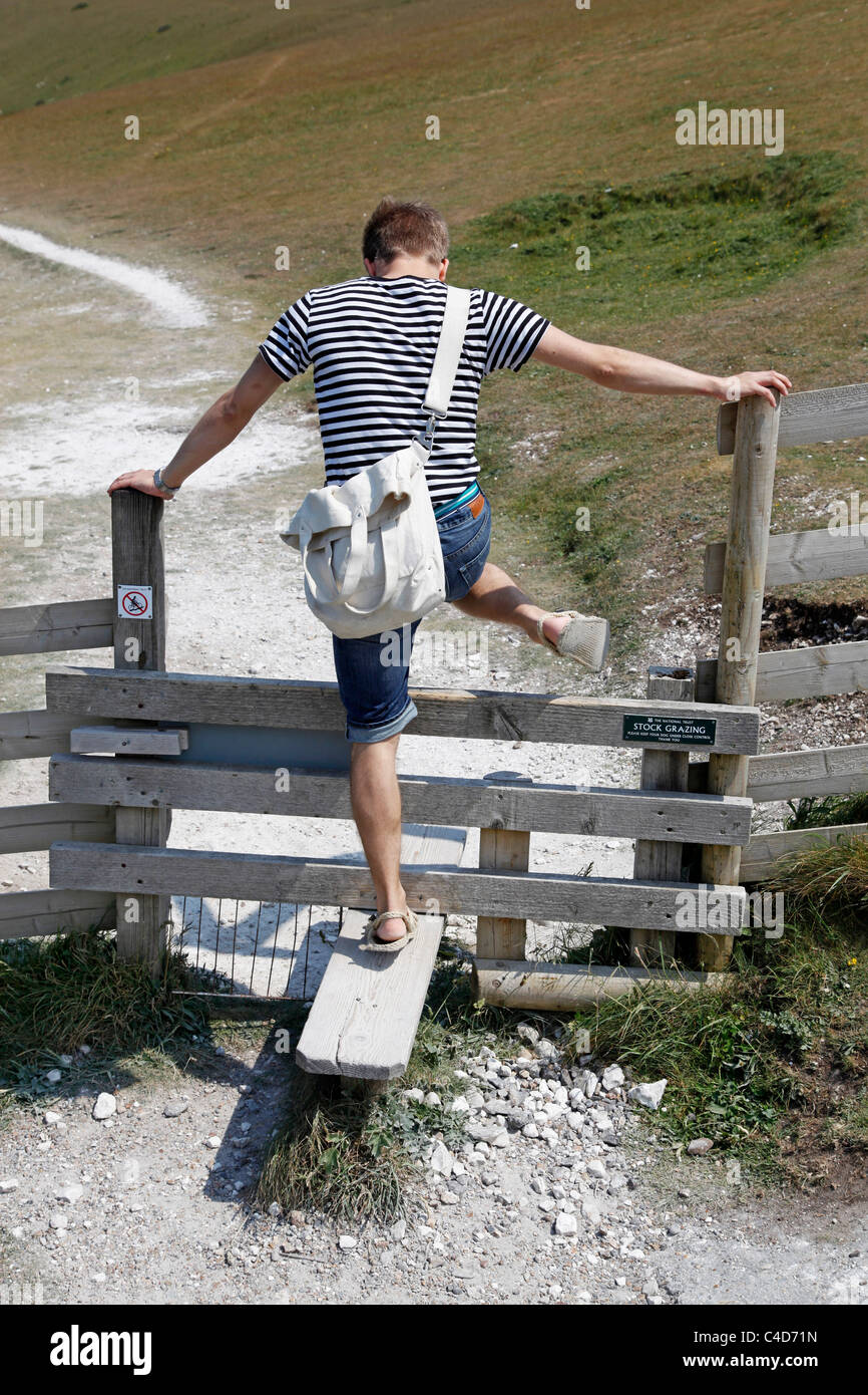 Man wearing striped T shirt on holiday stepping or climbing over a stile while walking along a path - Model Released Stock Photo