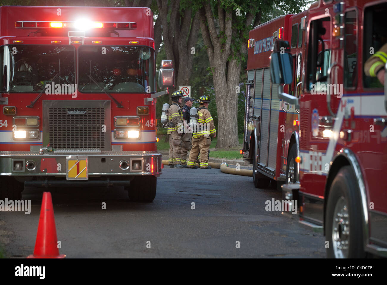 Firemen visible between fire trucks with emergency lights active whilst