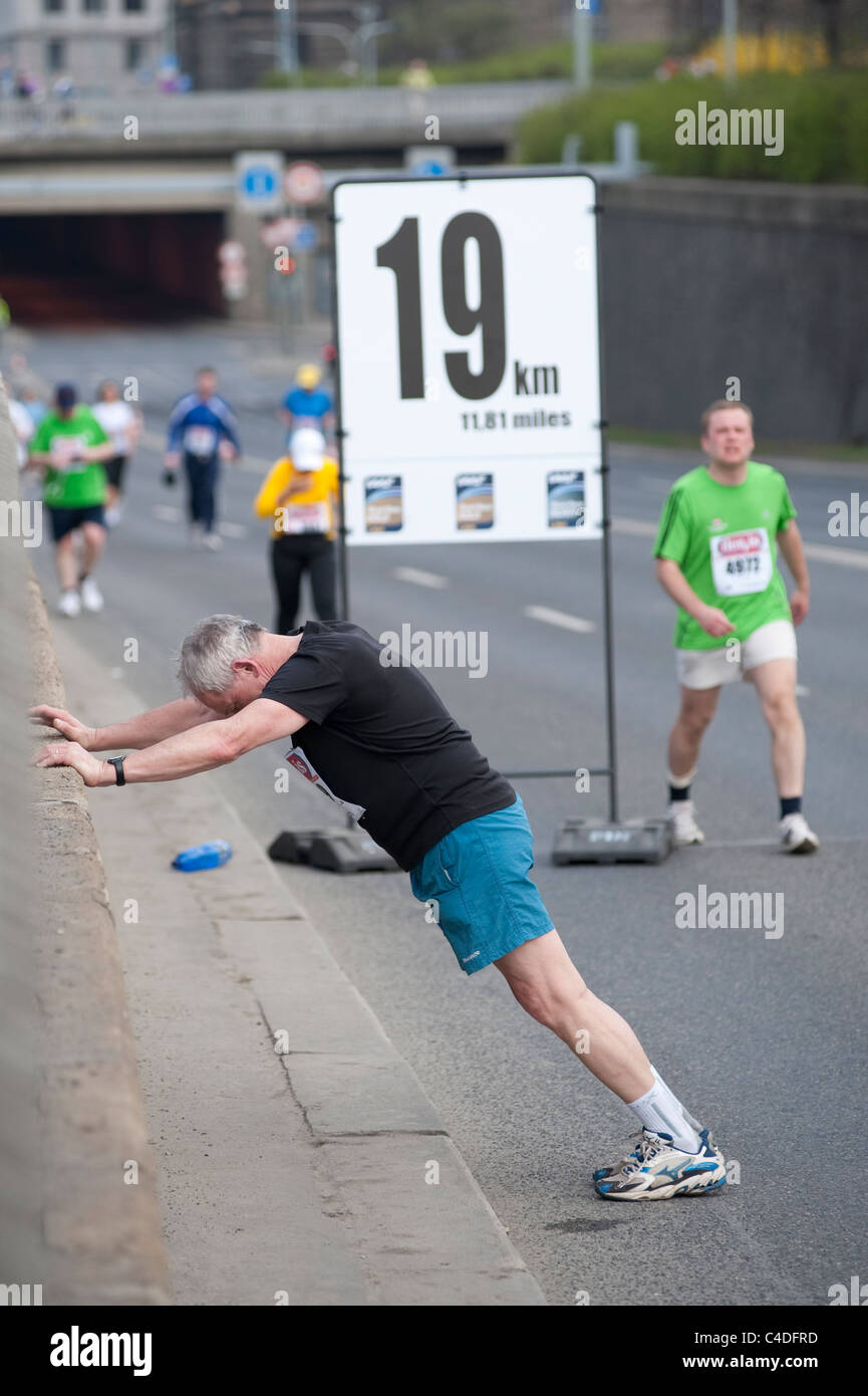 A tired runner with cramp leans against a wall and stretches his legs