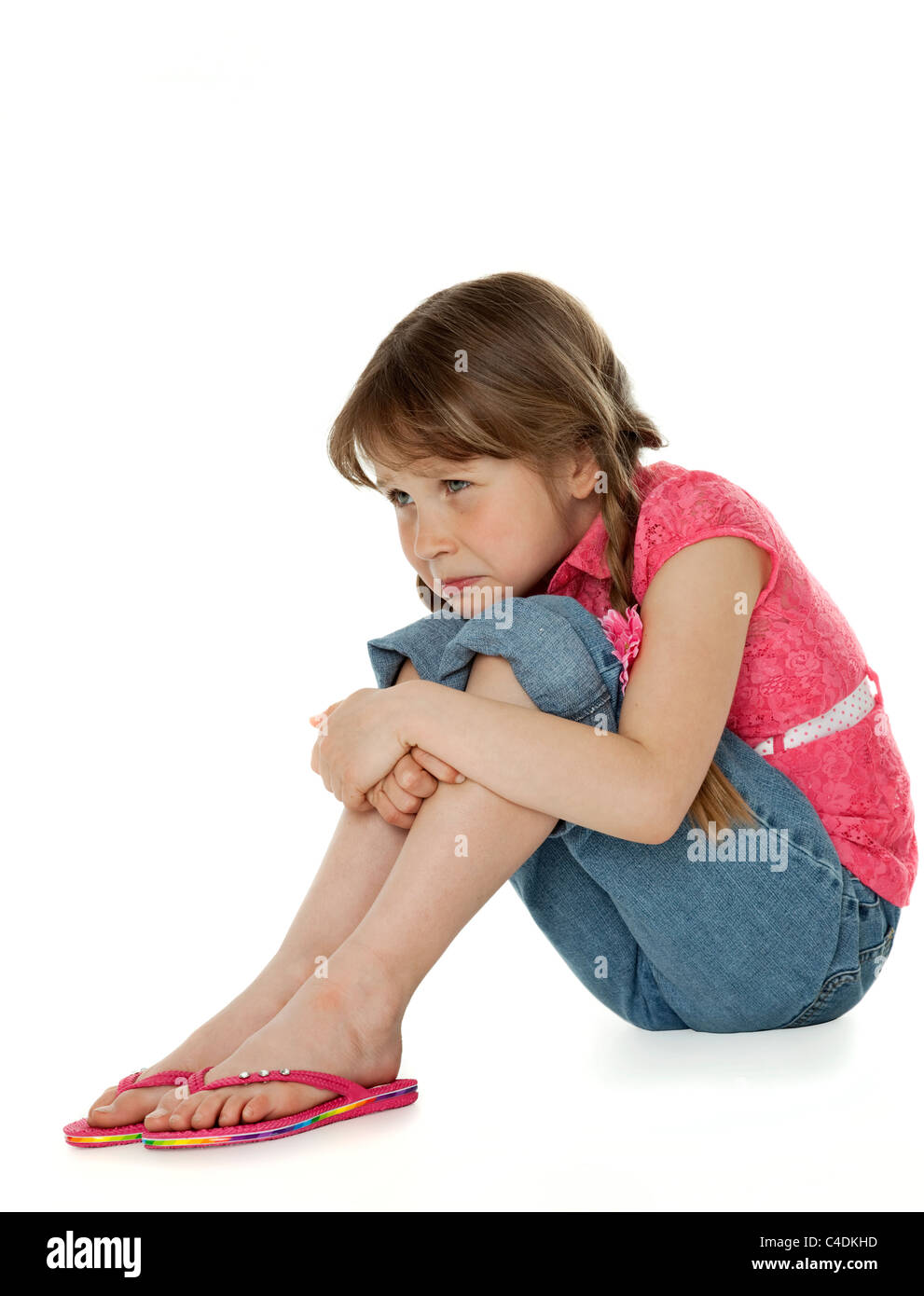 Young girl sitting, hugging knees, sad facial expression, on white