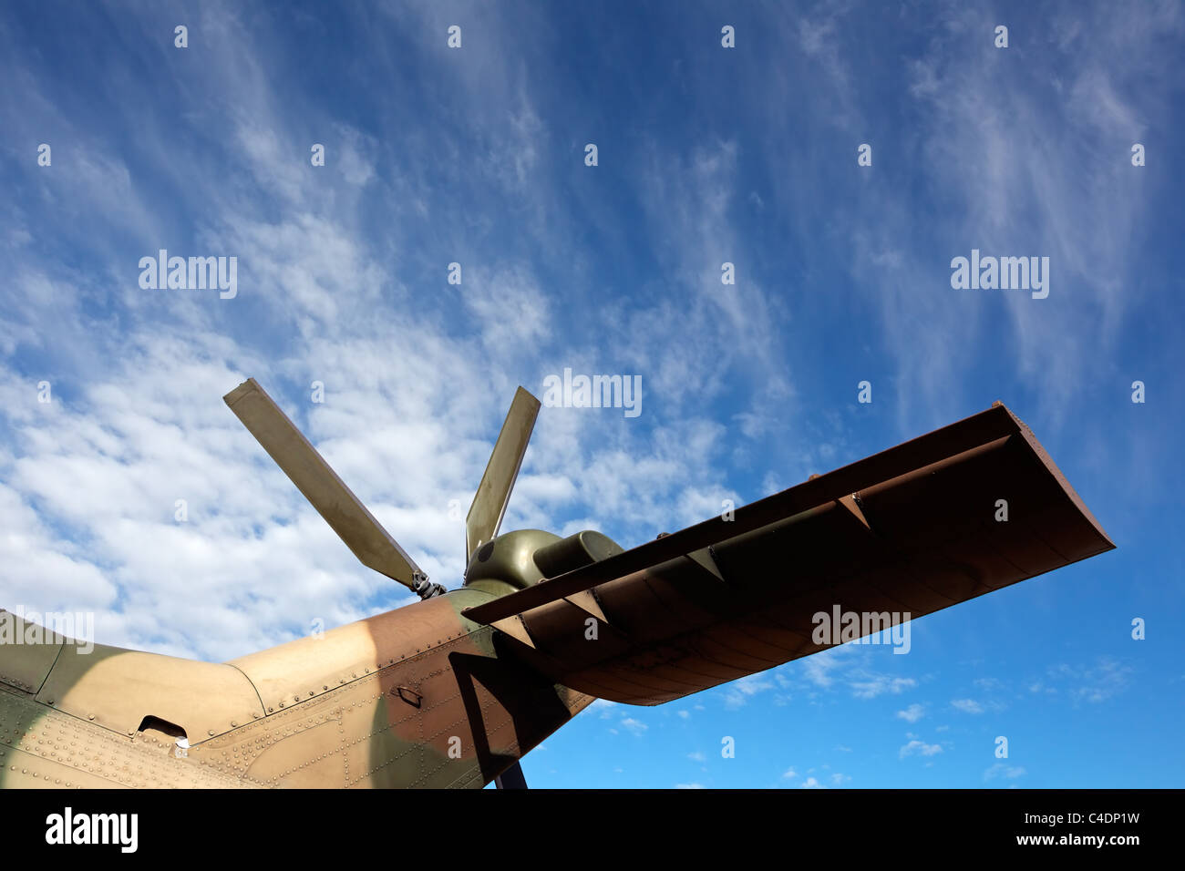 Tail rotor and tail wing of a military helicopter against a blue sky with clouds Stock Photo