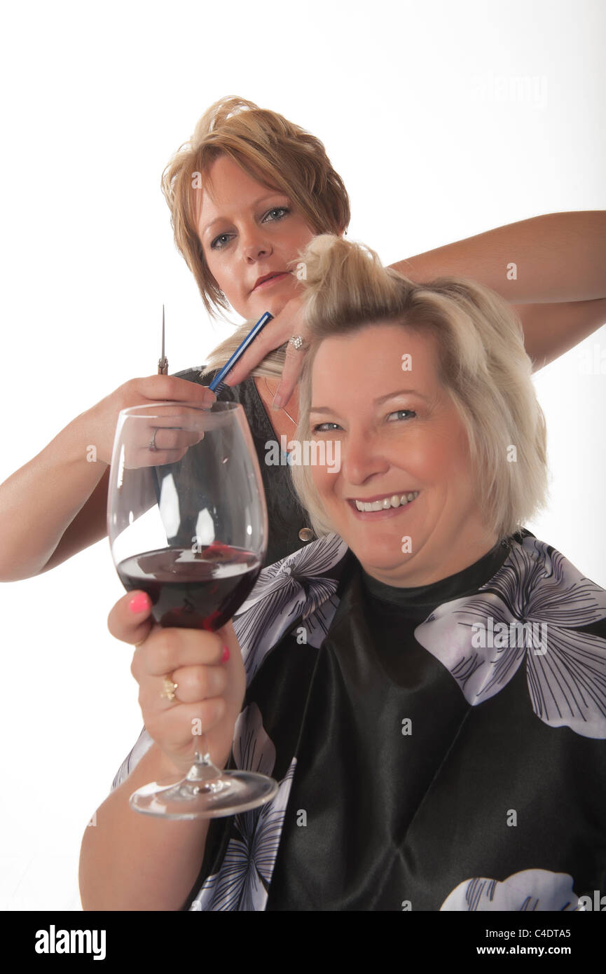 Hair stylist working on female customer with glass of red wine Stock Photo